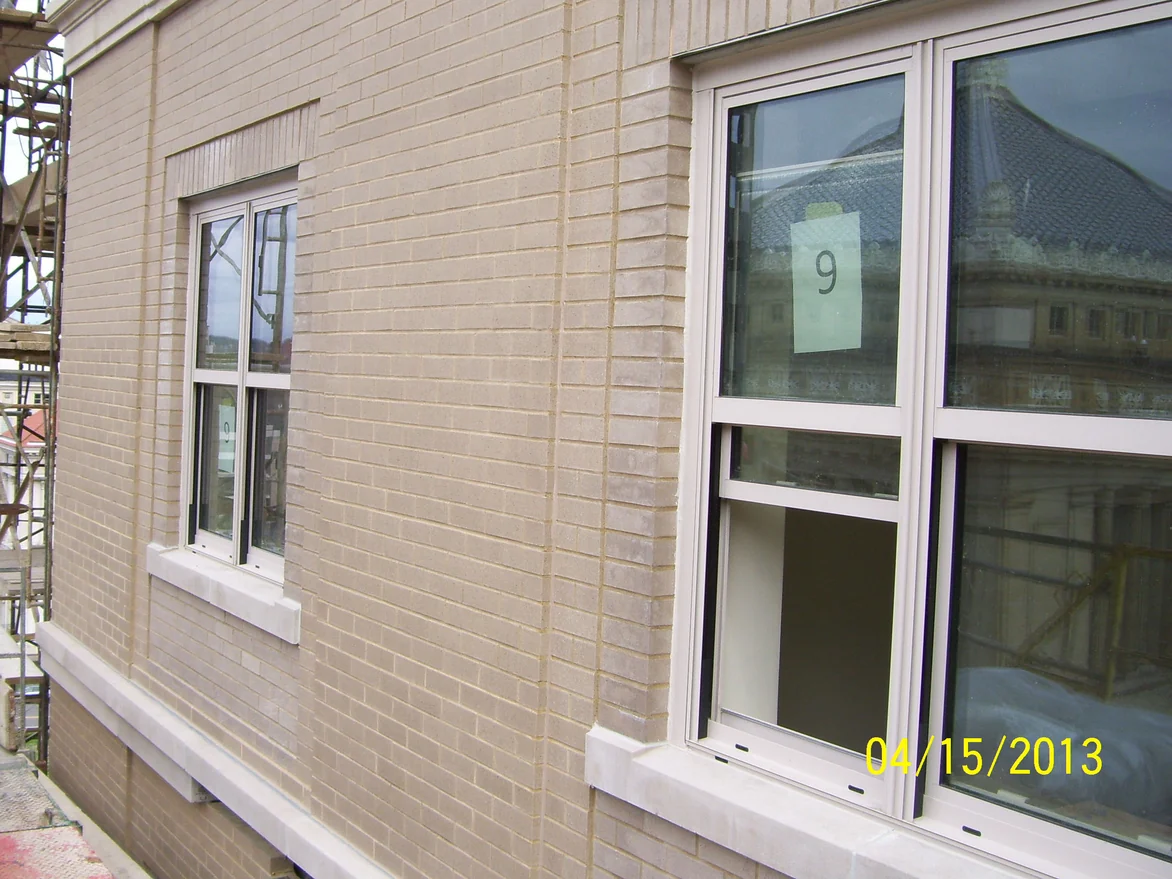 An oblique close view of the wall in 2013, its brick a pale tan with cast stone sills and a soldier course, a paper floor marker taped inside the window