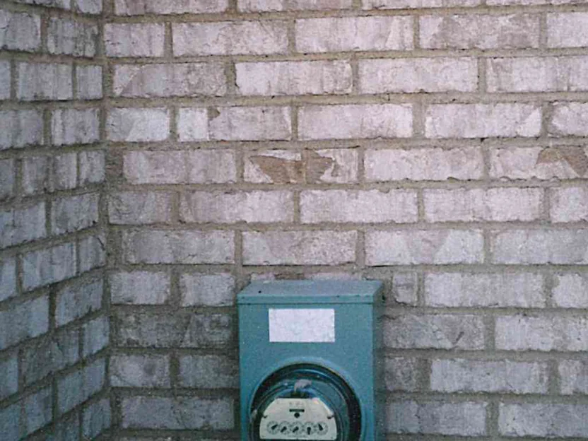 Close-up of an inside corner in 1997 above the electric meter, several brick with the textured face chipped away to show the red body underneath