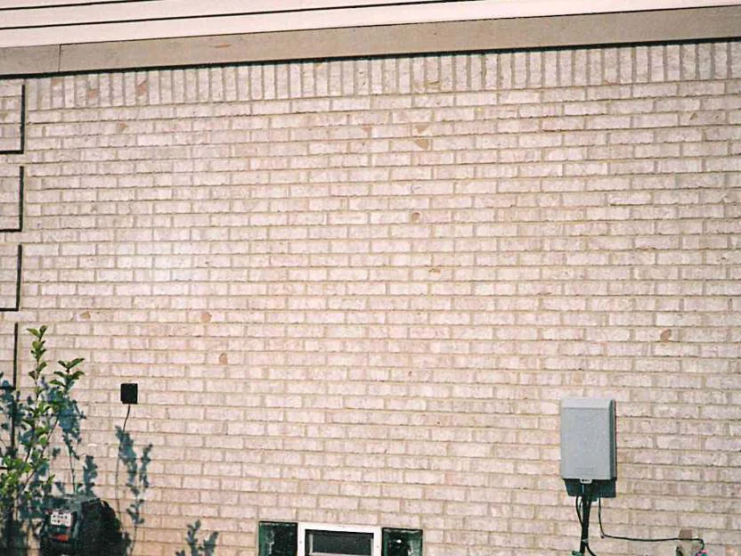 The side wall of the house in 1997, a scan of a film print, pale brick under a soldier course with darker chipped patches scattered across the face and a utility box at the lower right