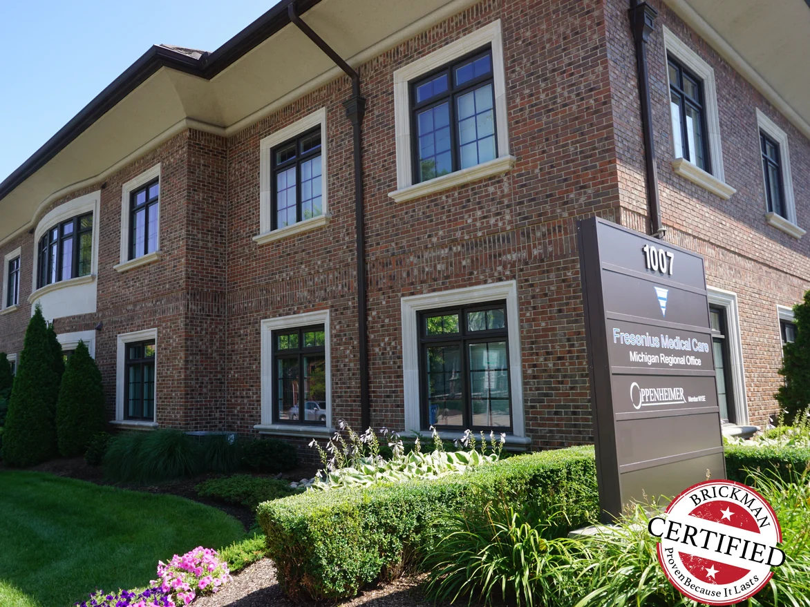 The same office building in 2019, its brick an even red and brown blend, with mature planting and a tenant sign at the kerb