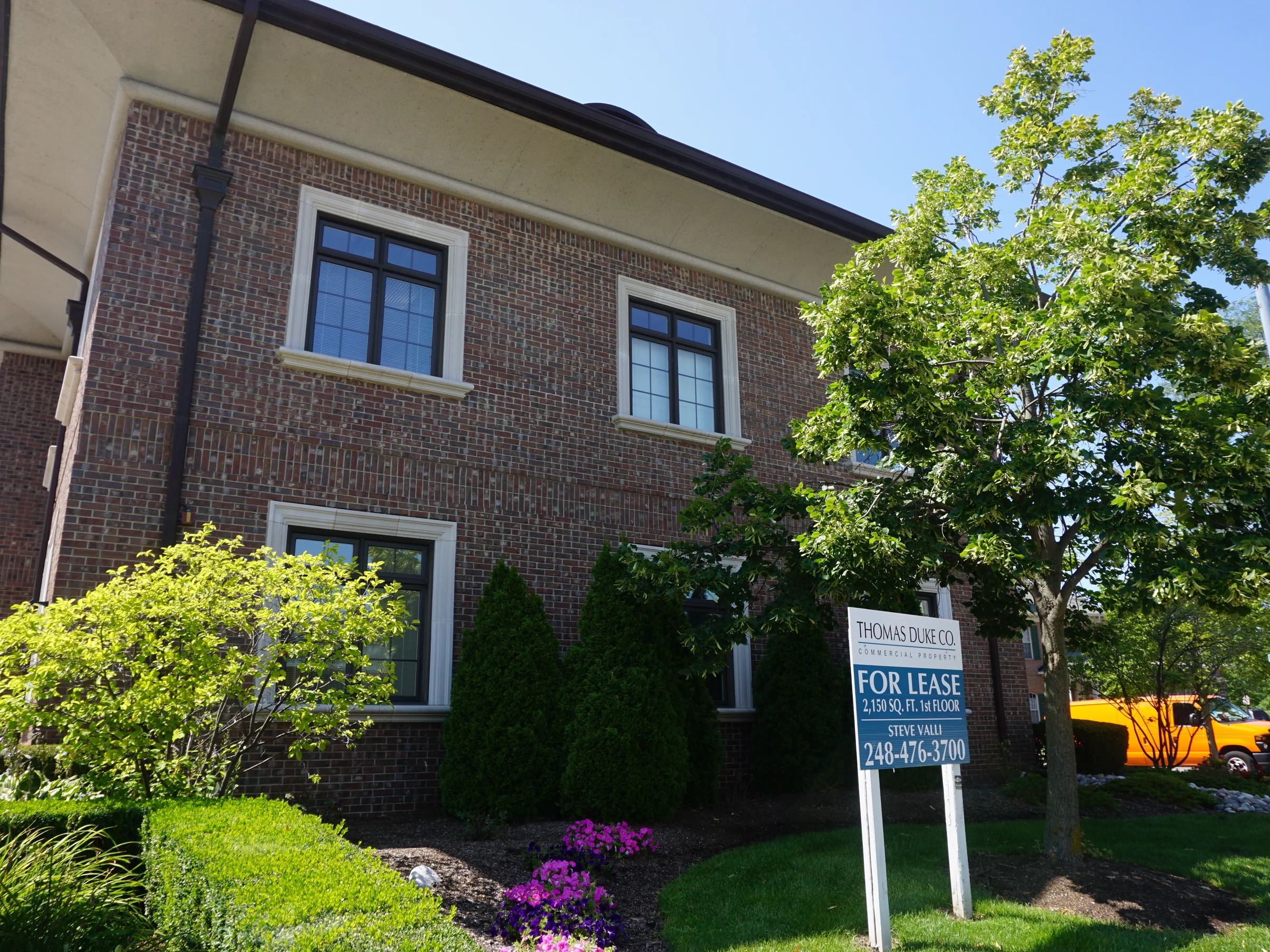 The office seen from the pavement across the front lawn, its blended brick reading as one consistent wall at distance