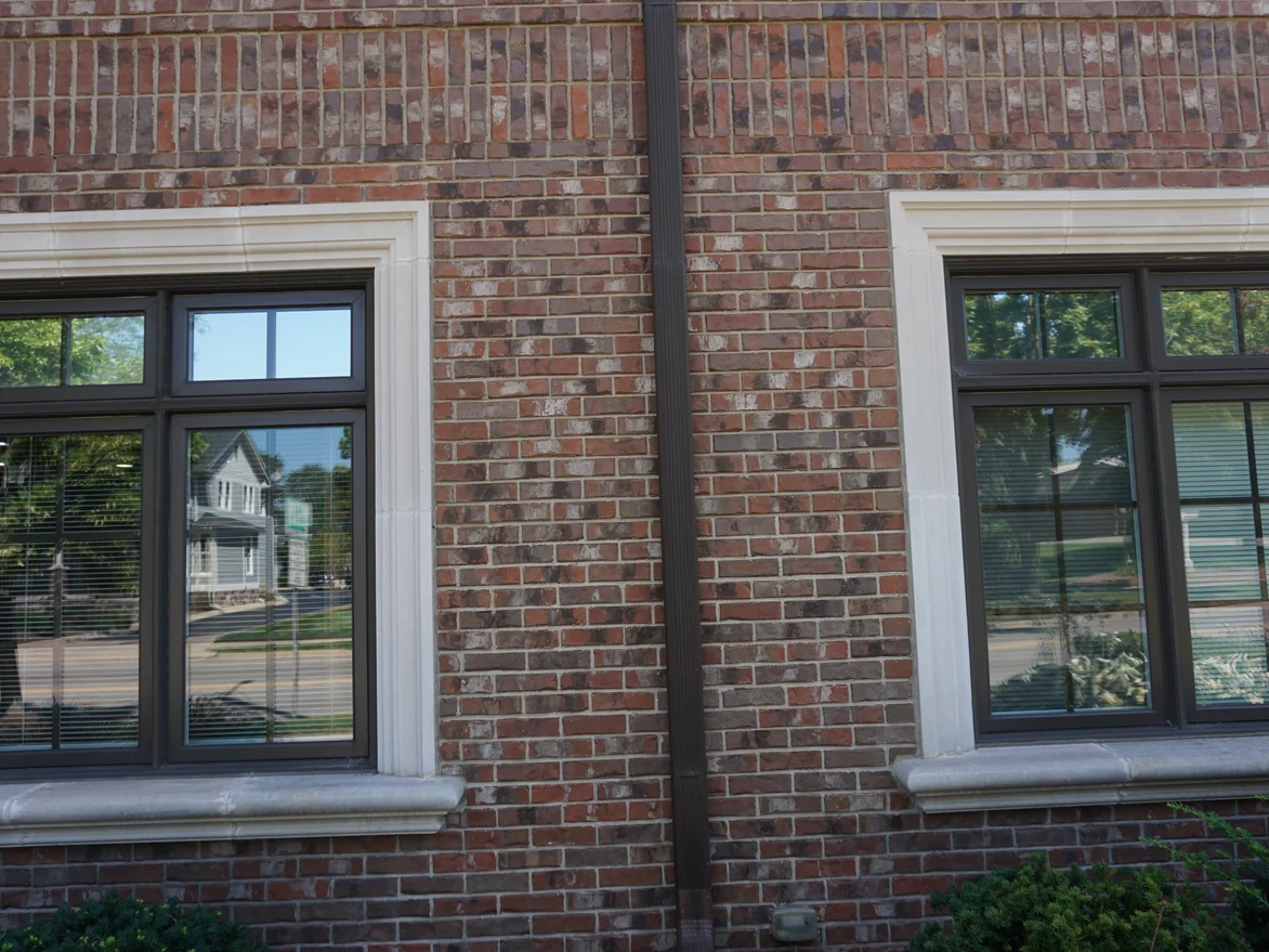 Two windows with cast stone sills and heads set in blended red and brown brick, with a soldier course running above them