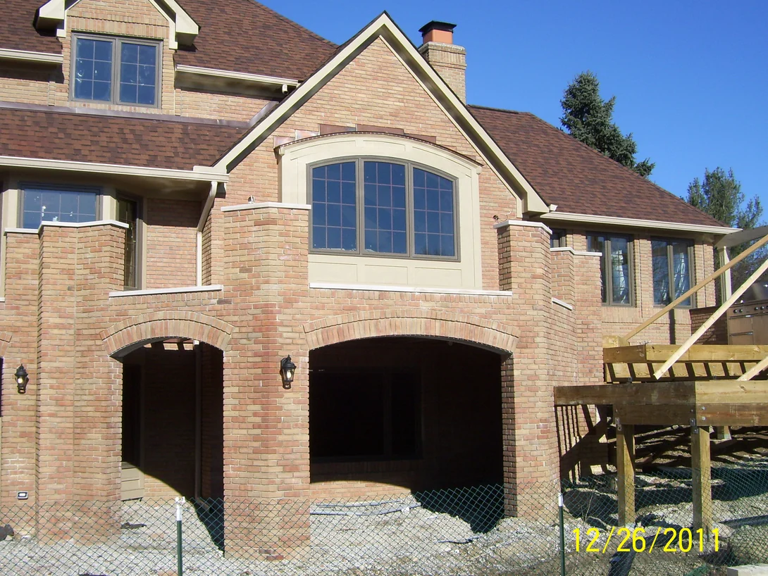 The back of the house under construction, its brick arches and column corners reading paler than the field brick around them
