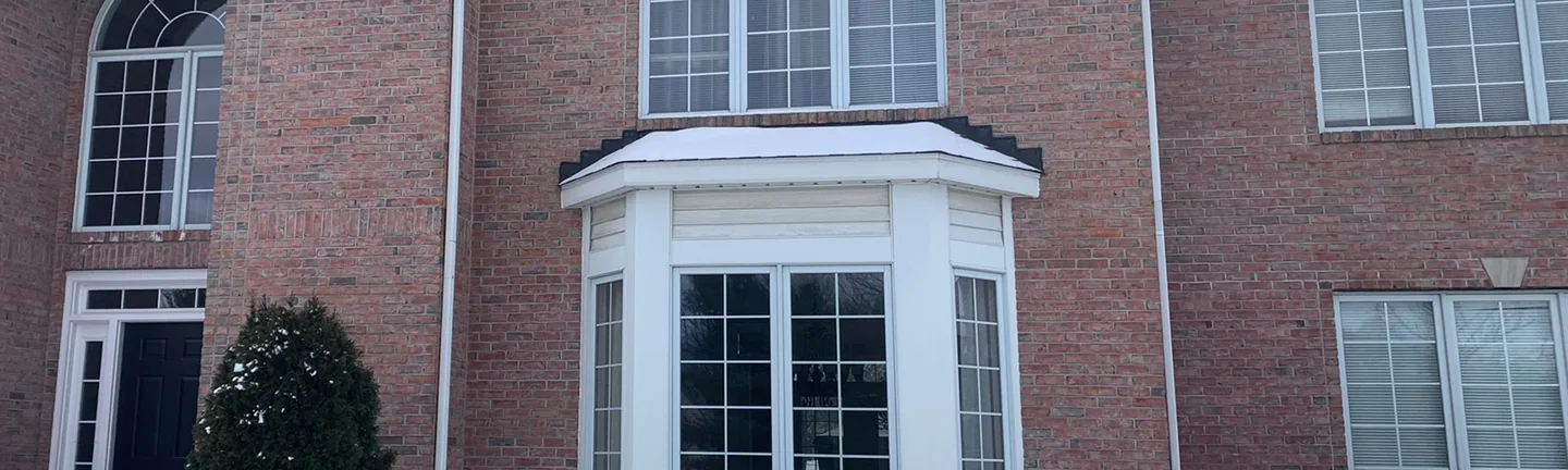 The front of the two-story brick house in 2021, its brick reading as one range from the arched entry across the bay window to the far wing
