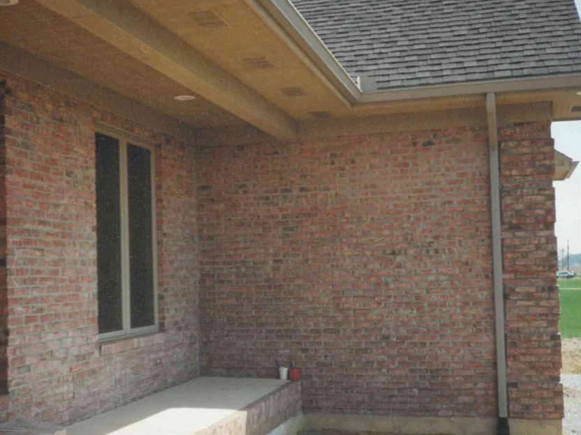 The same porch corner in April 1997 after staining, the brick reading one even red brown range from the window to the downspout, bare graded soil in front and a gable roof above