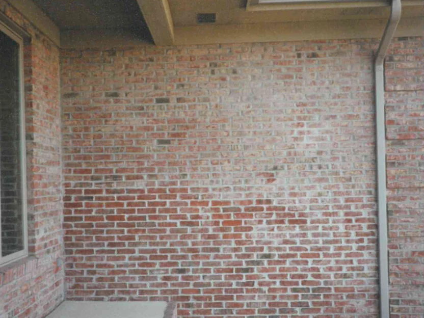 The porch corner of the new house in 1997, red brick under a heavy white haze across the whole wall beside a dark window, a downspout at the right