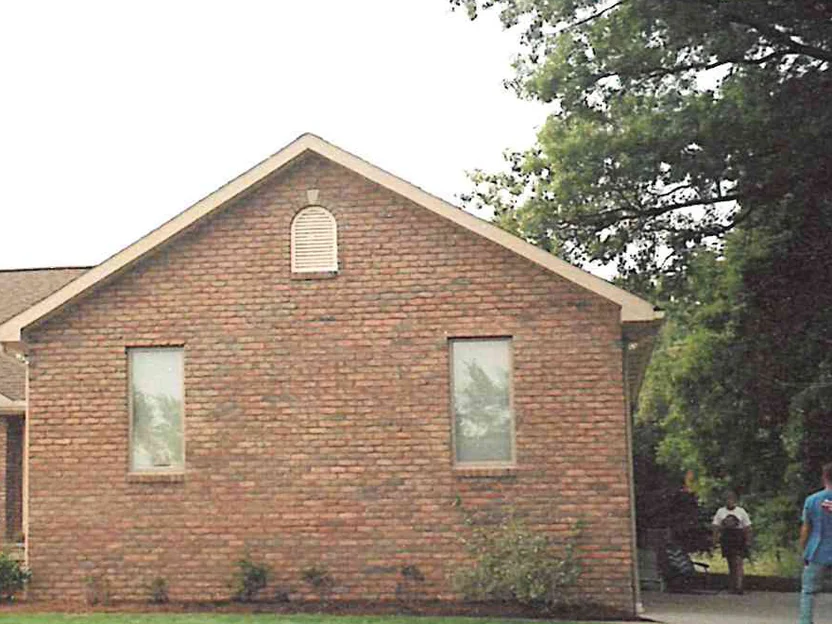 The same gable end later in 1999, the brick reading as one brown range from the planting bed to the ridge, with an extension ladder and a crew on the drive at the right