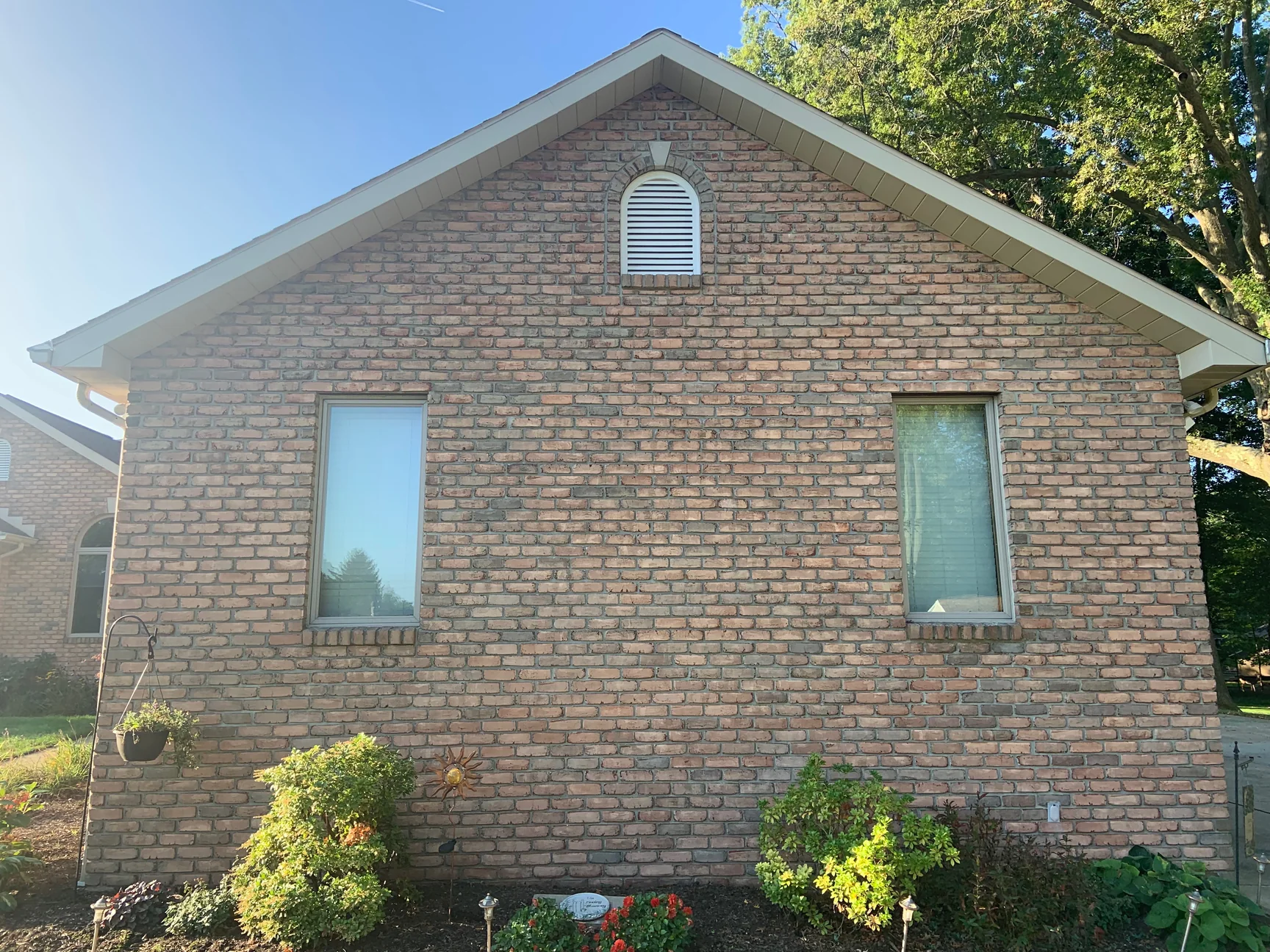 The same gable end in 2019, the whole wall holding one range of brick from the planted beds to the ridge, with a tall window either side of centre and a large tree beyond the right eaves