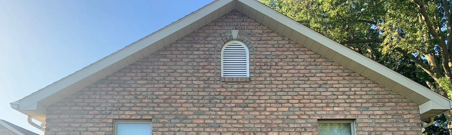 The gable end of the house in 2019, brick running as one range from the eaves up to the ridge around an arched louvre vent
