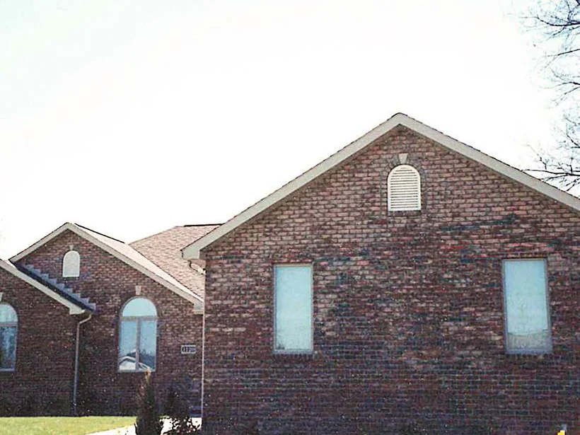 The gable end in 1999, the brick dark and mottled with large patches several shades off the courses around them, a bare tree at the right and fresh mulch at the foot of the wall