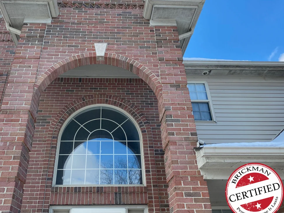 The entry arch of the Rochester Hills house in 2021, red brick from the gable down the pier in one range around the arched transom window, with the certification stamp in the corner.