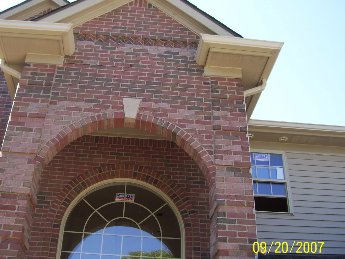 Looking up at the entry arch before staining, the brick a variegated mix of pink, red and purple grey under two cream corbels and a gable, with a burned-in camera date of 09/20/2007