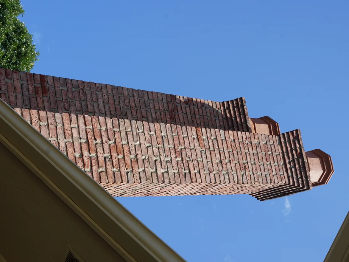 A corbelled brick chimney breast and its clay pots seen from below against a clear sky