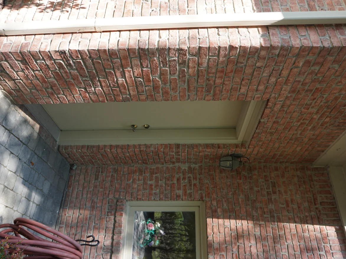 The covered entry seen from below, a brick jack arch and soffit over the door with a lantern on the wall beside it
