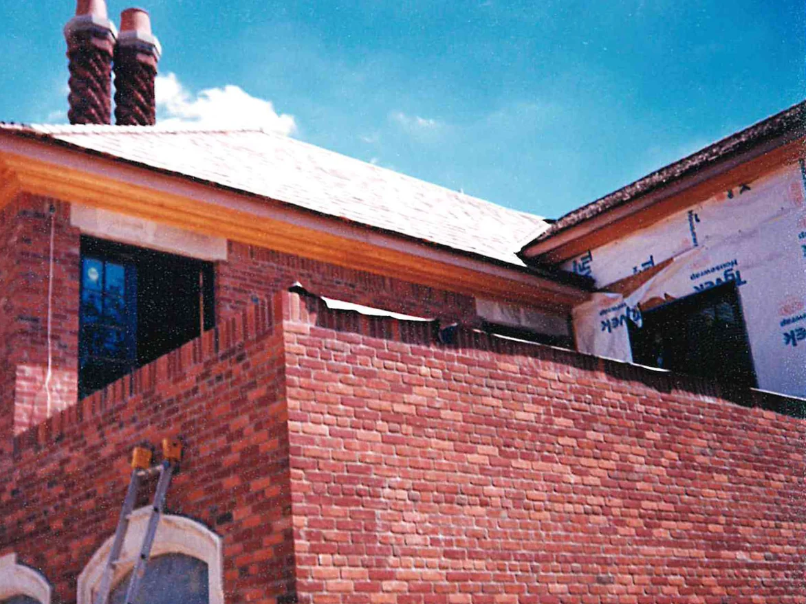 The gable end and twin chimney of the house under construction in 1997, with a ladder standing against the wall