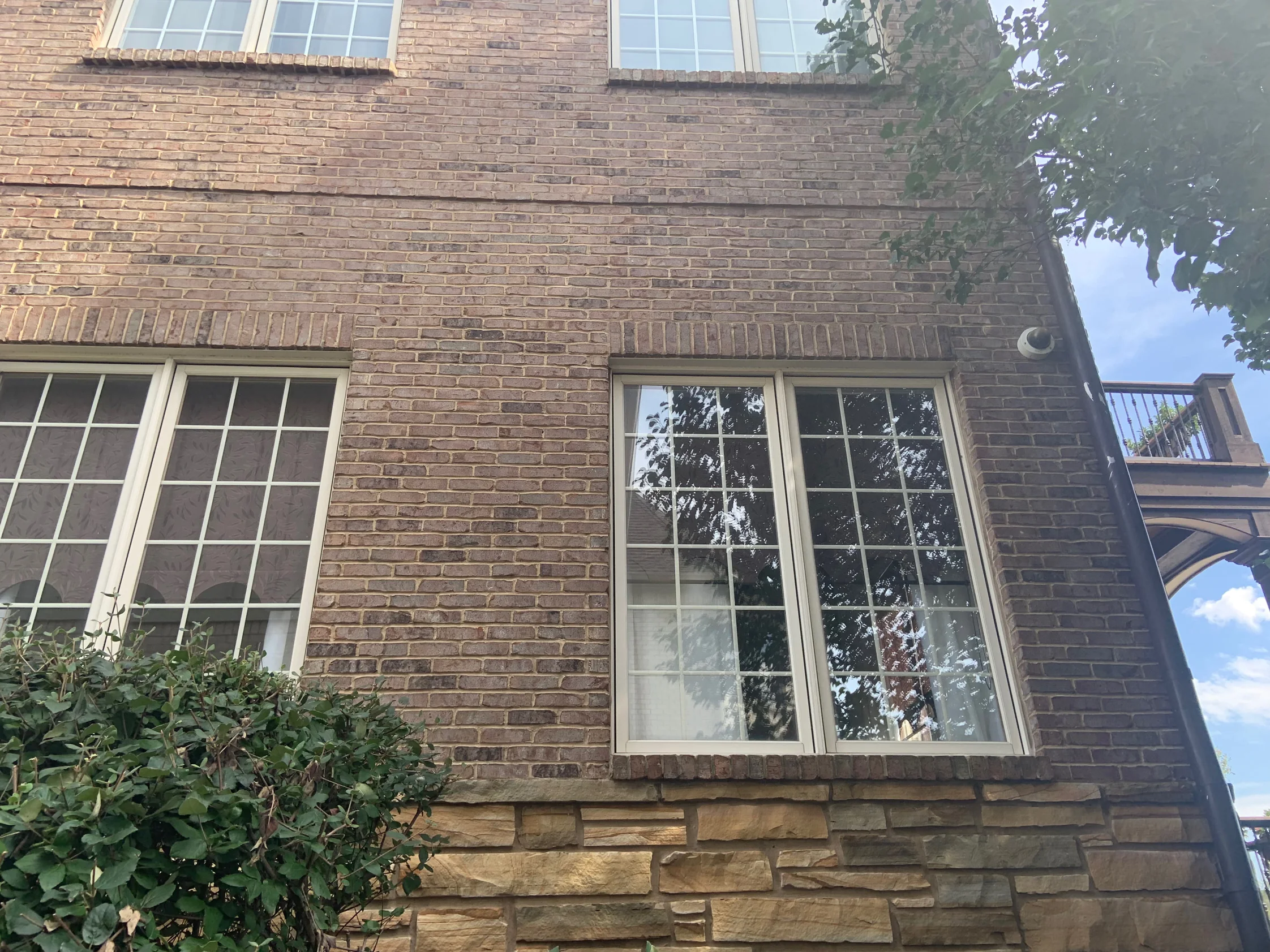 Close view of the brick and its mortar joints in 2019, tan and brown units running down to the sandstone base beside two windows