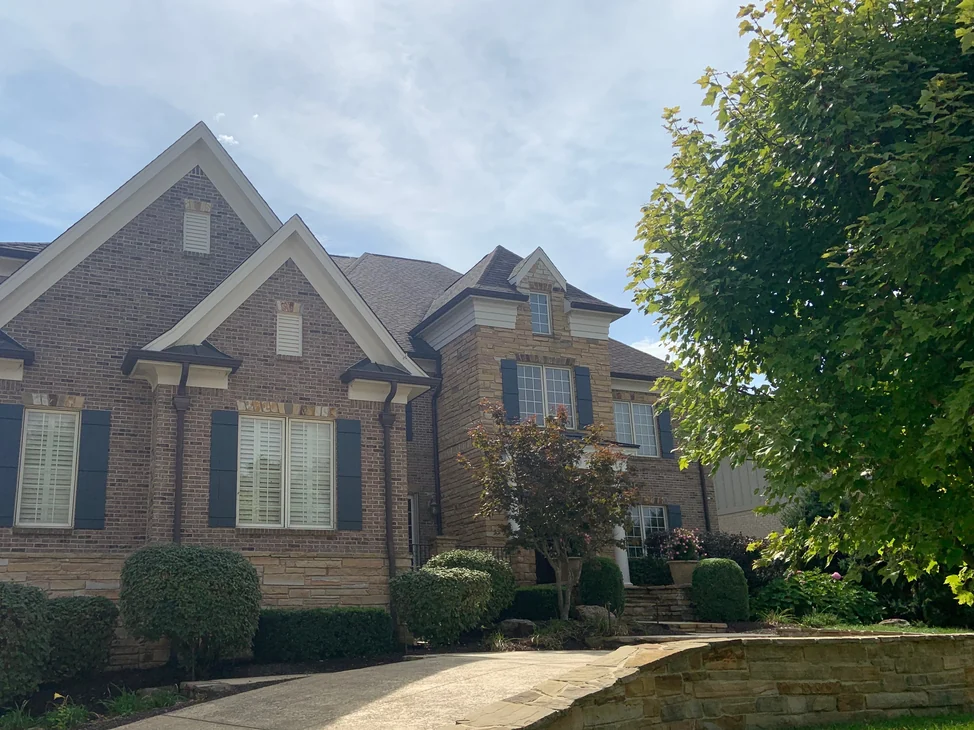 The front of the house in 2019 from the driveway, its twin brick gables and stone bay reading as one settled range under mature planting.