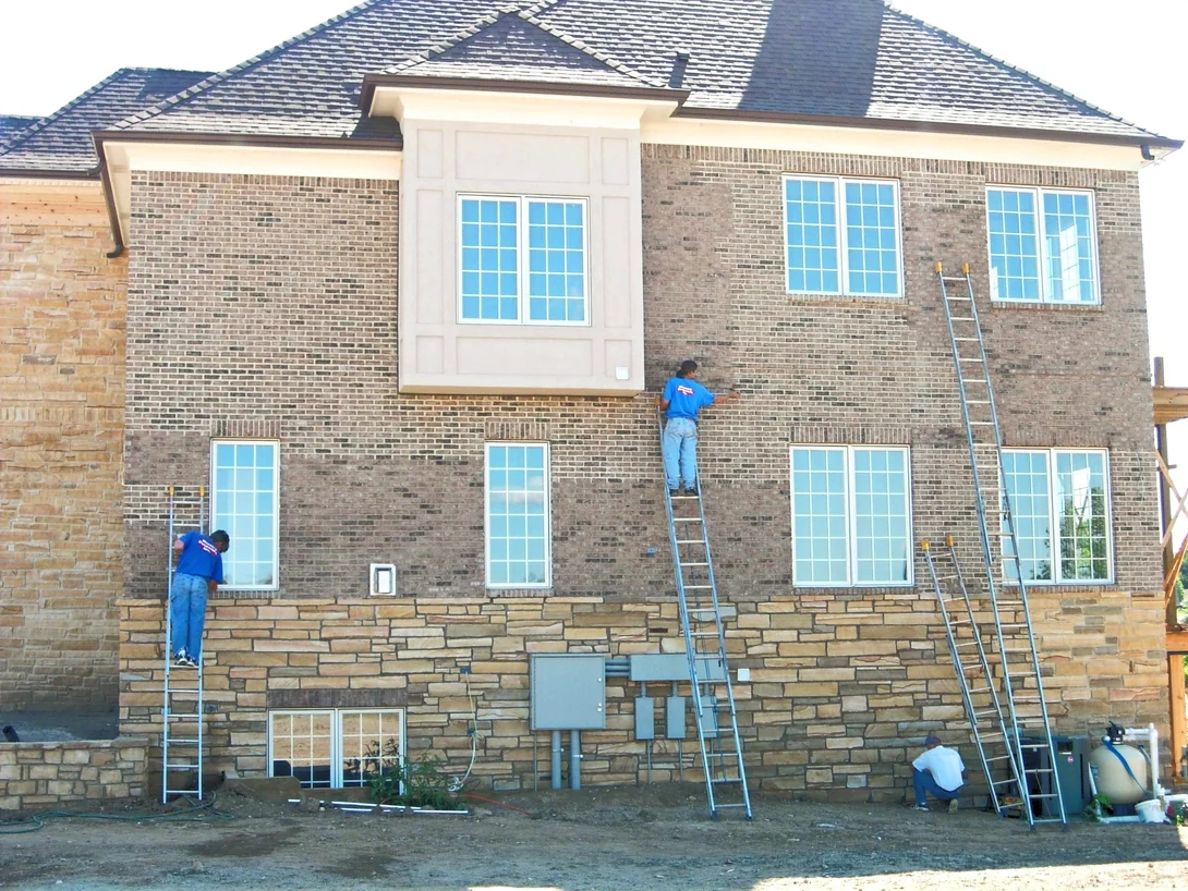 Two applicators on ladders working across the rear elevation of the house in 2007, the brick a mixed grey and brown above a sandstone base