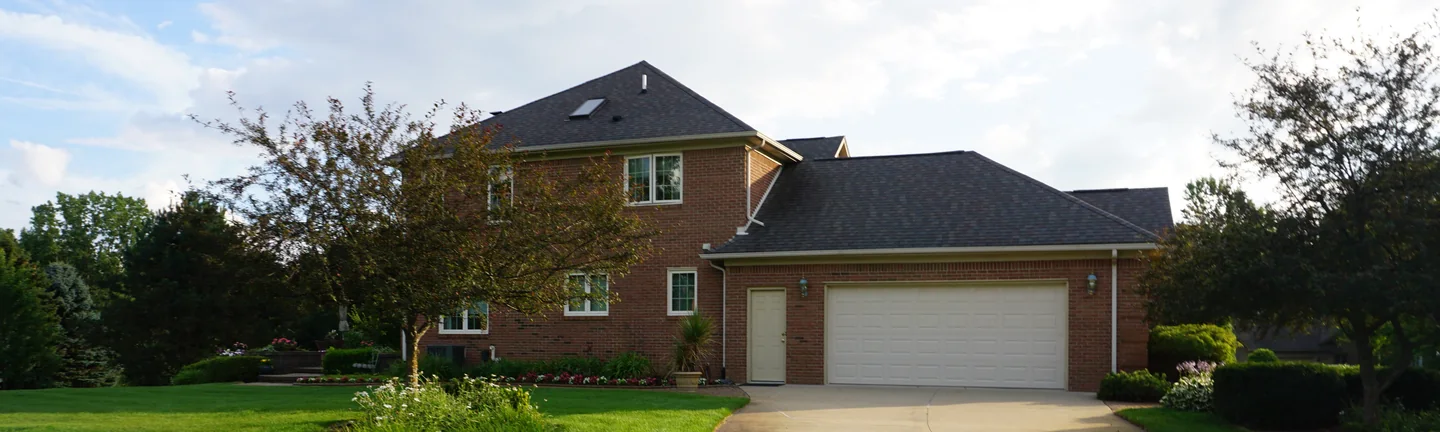 A two-story brick house seen across its front lawn in 2019, the brick one even red range from the gables down to the garage