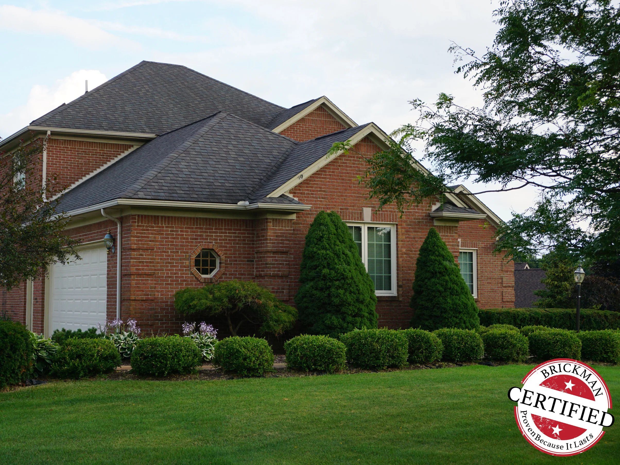 The same gable and octagonal window in 2019, the brick one consistent red range from the peak down to the garage door, the Brickman certified stamp in the corner of the frame
