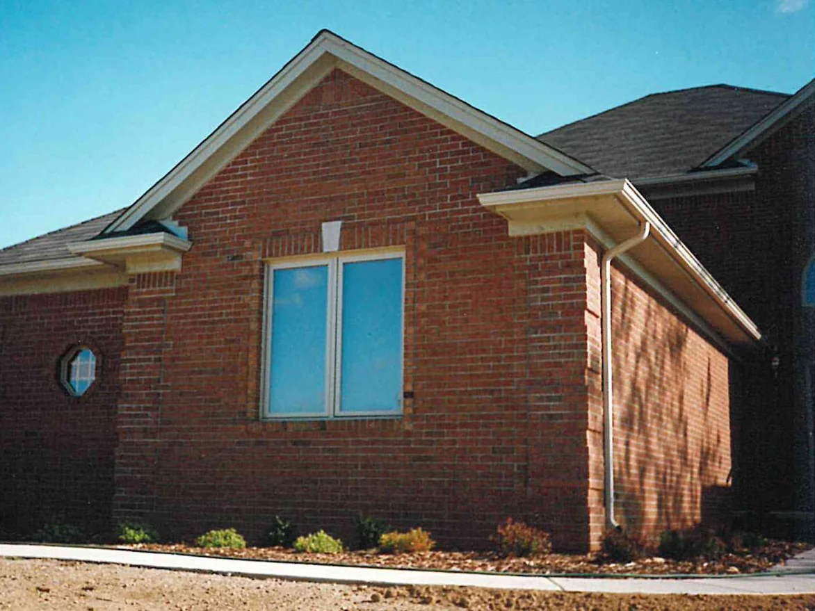 The gable end of a newly built house in 1996, pale units scattered through the red brick around an octagonal window, bare soil where the lawn will go