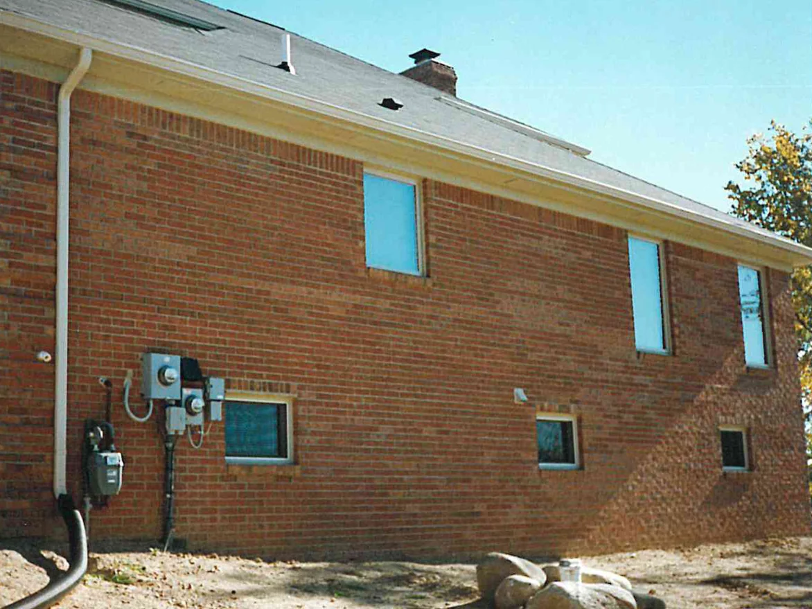 The long side wall of the same house in 1996, the gas and electric meters mounted low on brick that runs from red to pale tan across the elevation