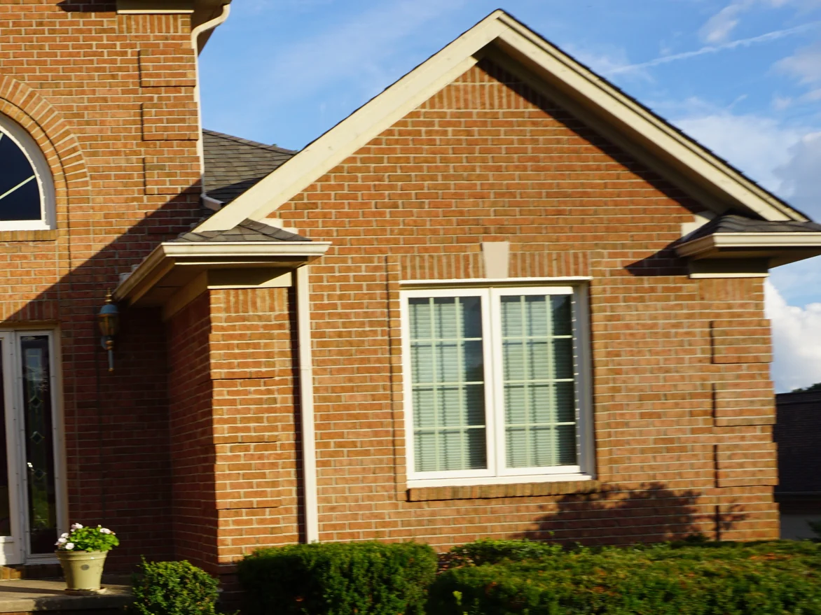 The gabled entrance wing in low evening sun in 2019, cast stone accents set into evenly ranged brick above a bank of clipped boxwood