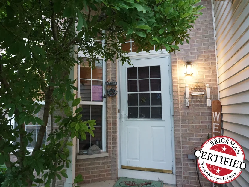 The front door in 2019 under a lit carriage lantern, the brick around it pale and even, with the certification stamp in the corner
