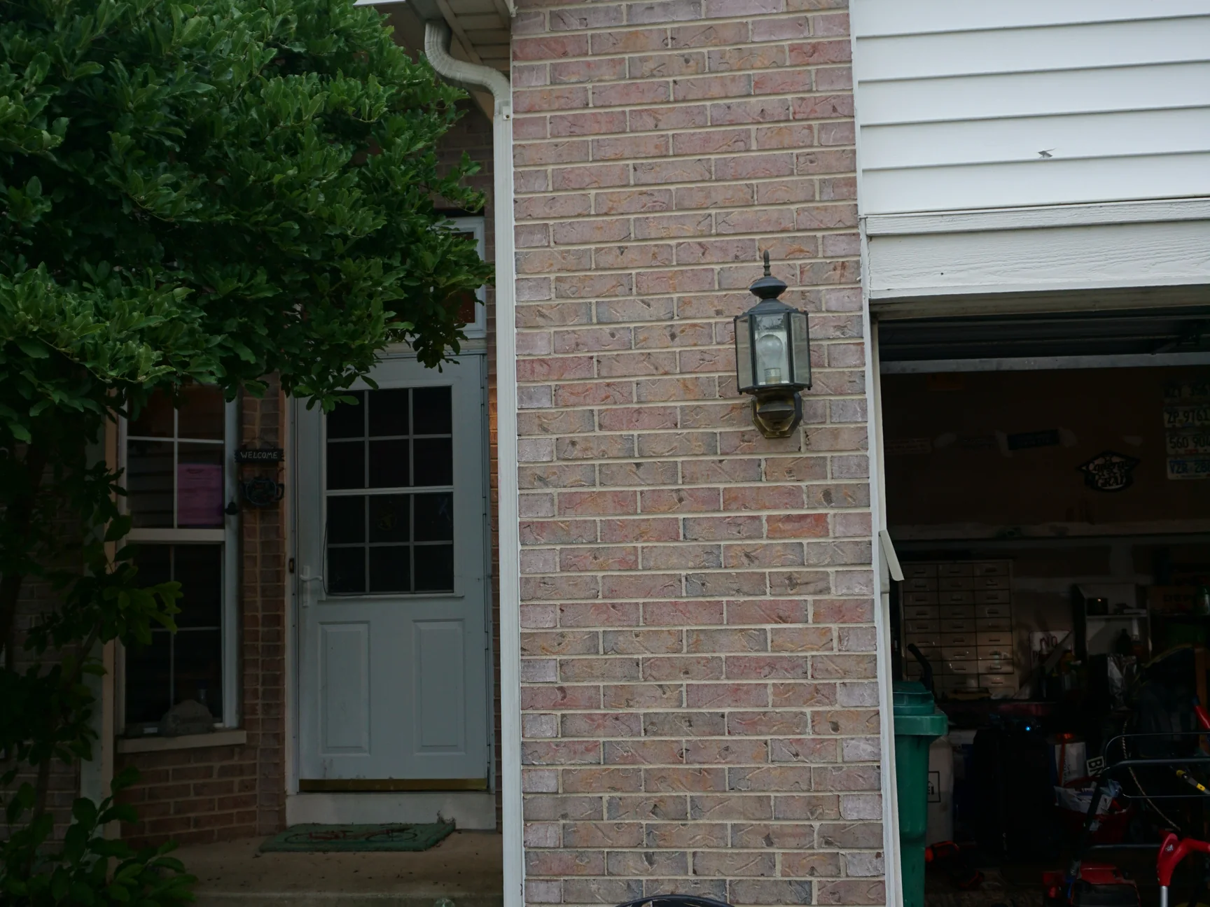 The front of the house in 2019, the brick pier between the entry and the open garage reading as one pale pink and buff blend