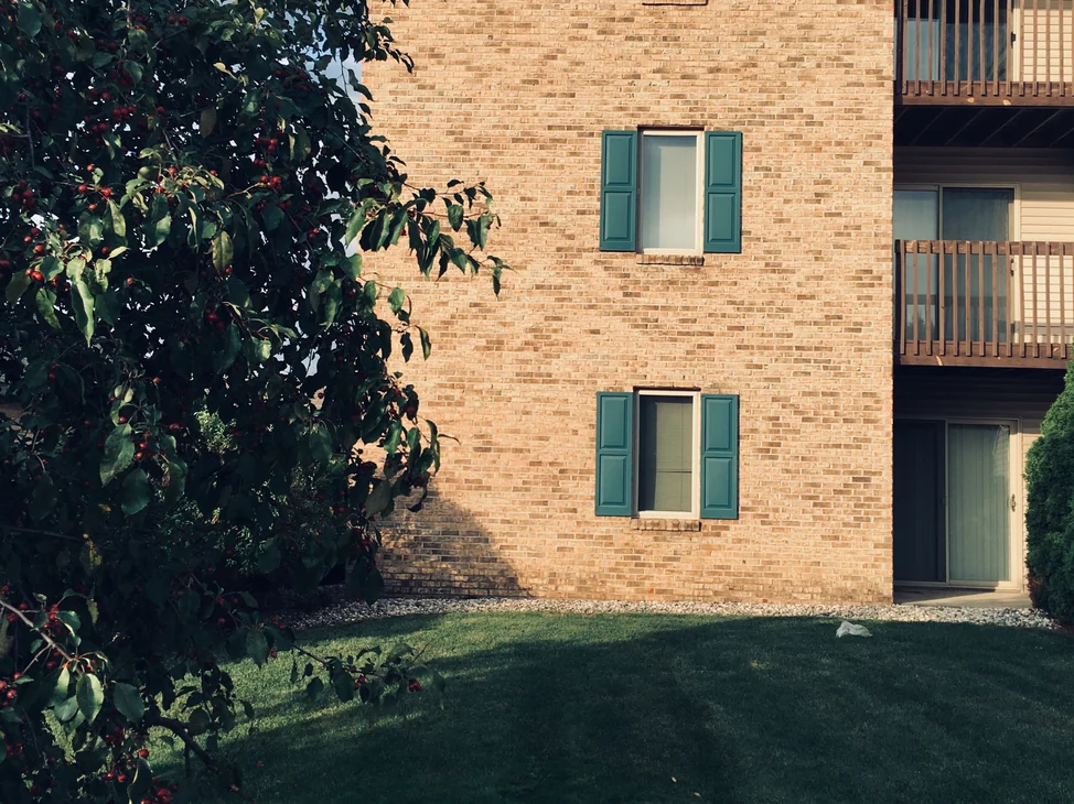 An apartment building at Royal Vista in 2019 seen across the lawn past a crabapple tree, its brick one even buff range with timber balconies down the right side.