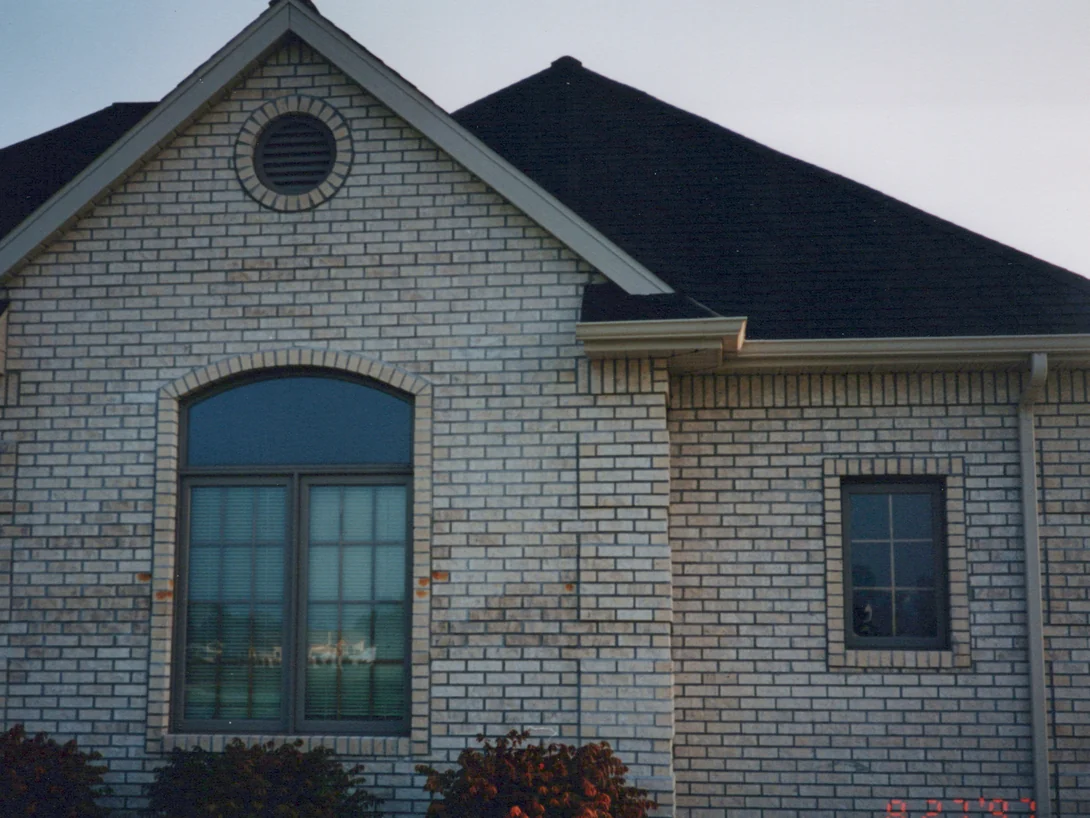 The front gable in 1997, an arched window under a round louvred vent, the tan brick mottled with darker units and a camera date stamped in the corner