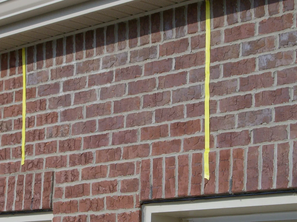 The brick over the garage doors in 2007, two strips of yellow tape hanging down the wall below the soffit to mark off a run of lighter units