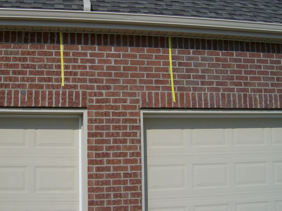 The two garage doors and the pier between them in 2007 with the tape still on the wall, the top courses under the soffit reading darker than the brick below