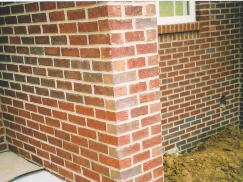An outside corner in 2003, the pier brick several shades lighter and pinker than the wall it turns into, with bare graded dirt piled at the base