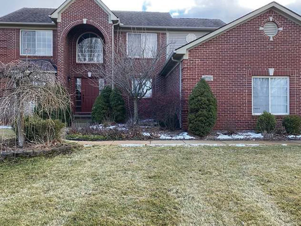 The front of the two-story house in Saline in 2020, red brick reading as one range across the arched entry and the gabled wing, above a grown lawn.