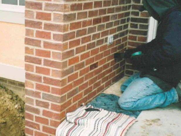 An applicator kneeling on the entry slab in 2003, working stain into the brick by hand with a cloth laid out beside him, dated November 17