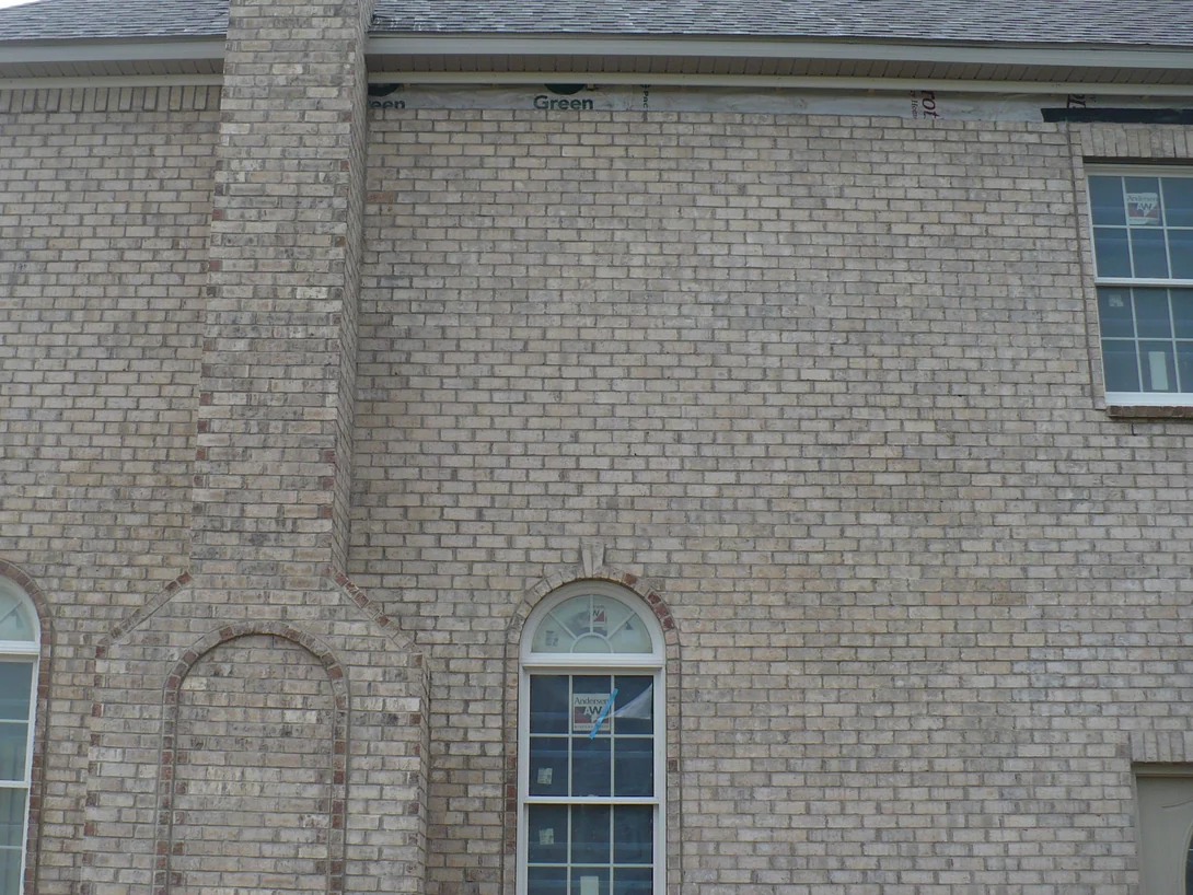 The chimney side of the house in 2012 after the dark units were lightened, buff brick reading one range from the arched windows up to the eave, with house wrap still showing under the soffit