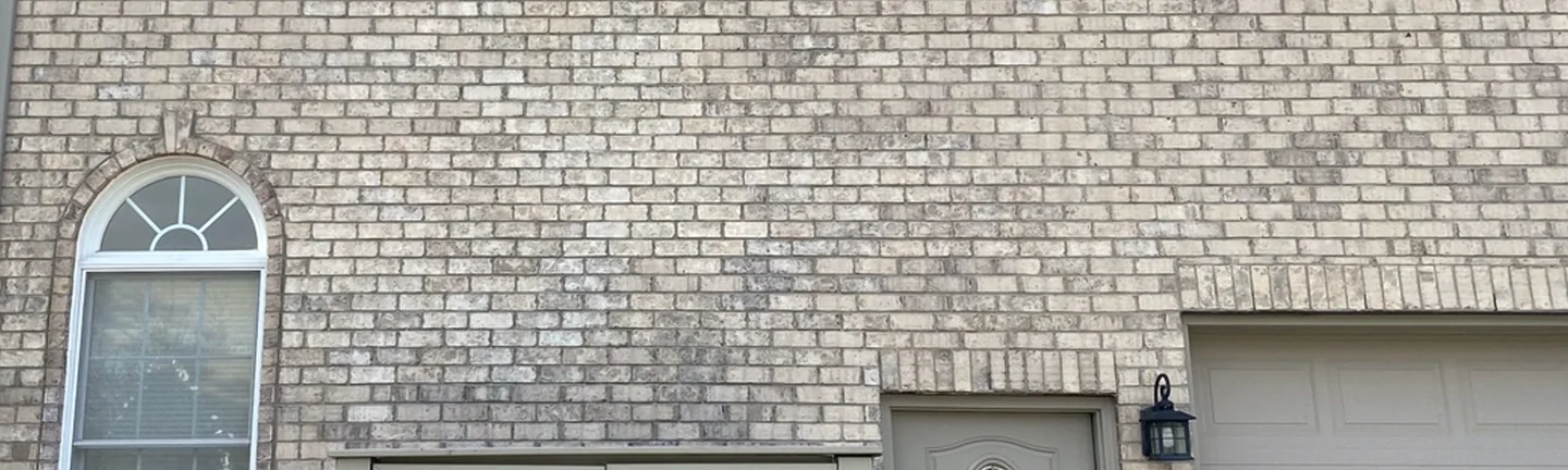 The garage wall of the Saline house in 2020, buff brick reading as one range from the arched window across to the garage door
