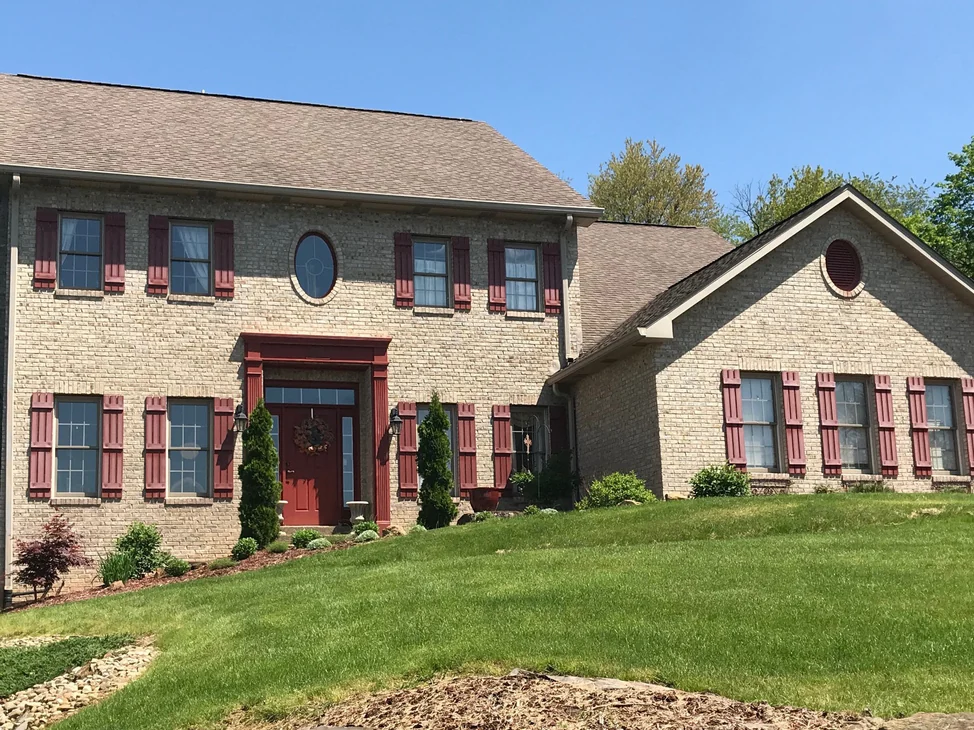A two-story brick home in 2019, its walls one even color under dark red shutters