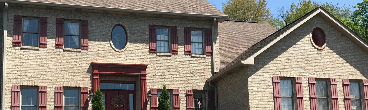 The brick front of a two-story home in 2019, one even color across the wall under a row of shuttered windows