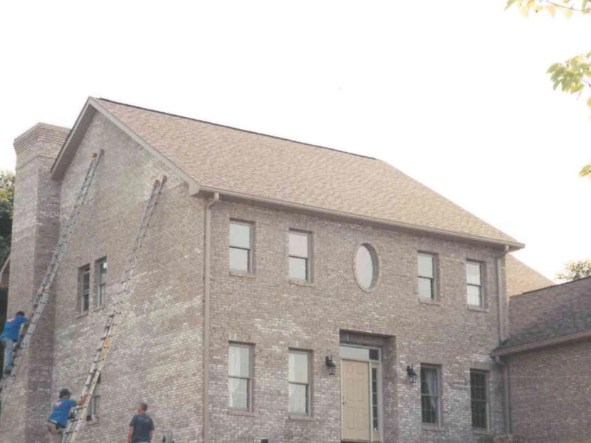 Three applicators on ladders working across the front of the two-story house, its brick still pale and blotched