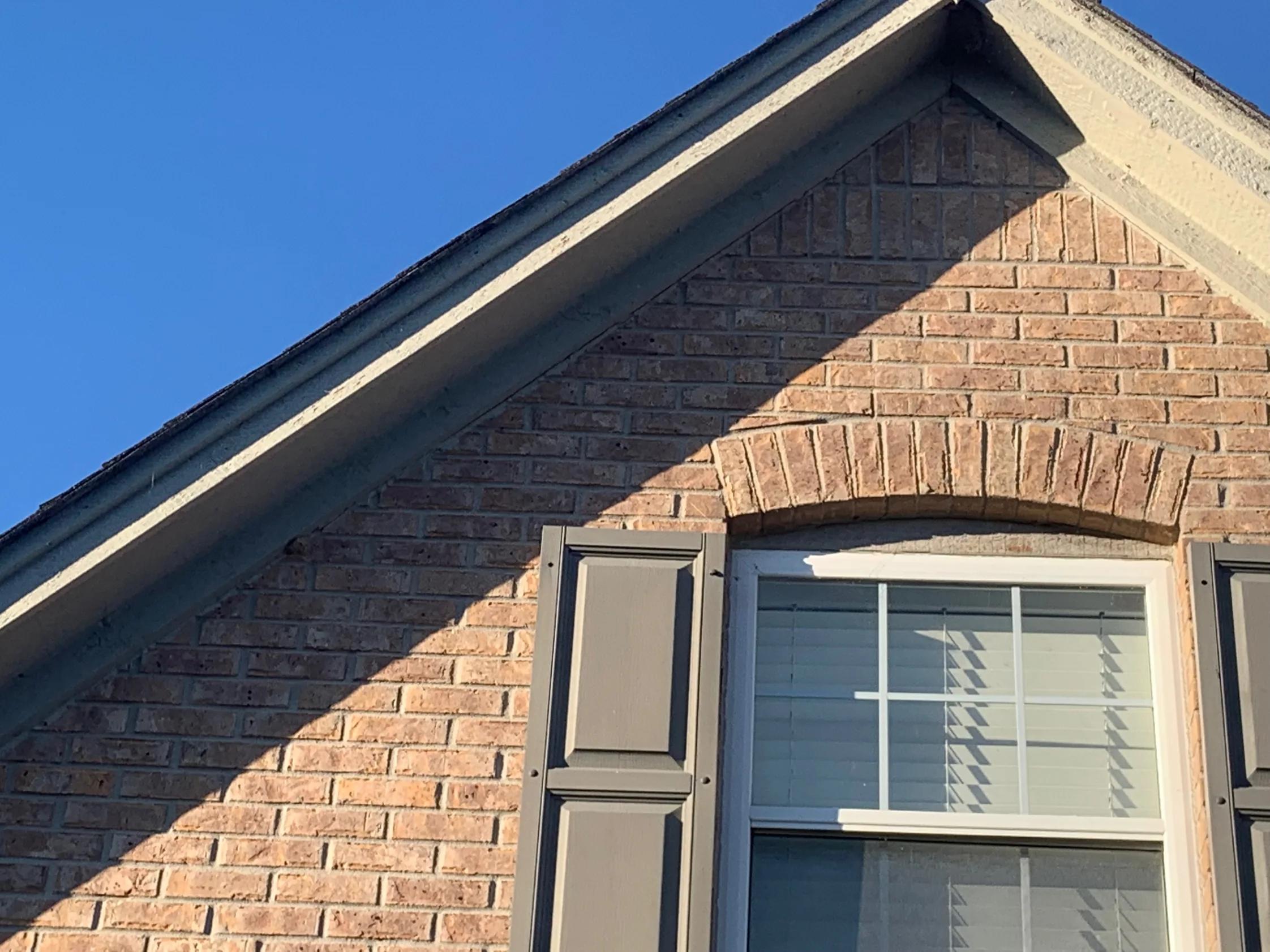 Close view of the brick arch over a gable window in 2019, tans, browns and pale creams running through the courses with pale mortar joints