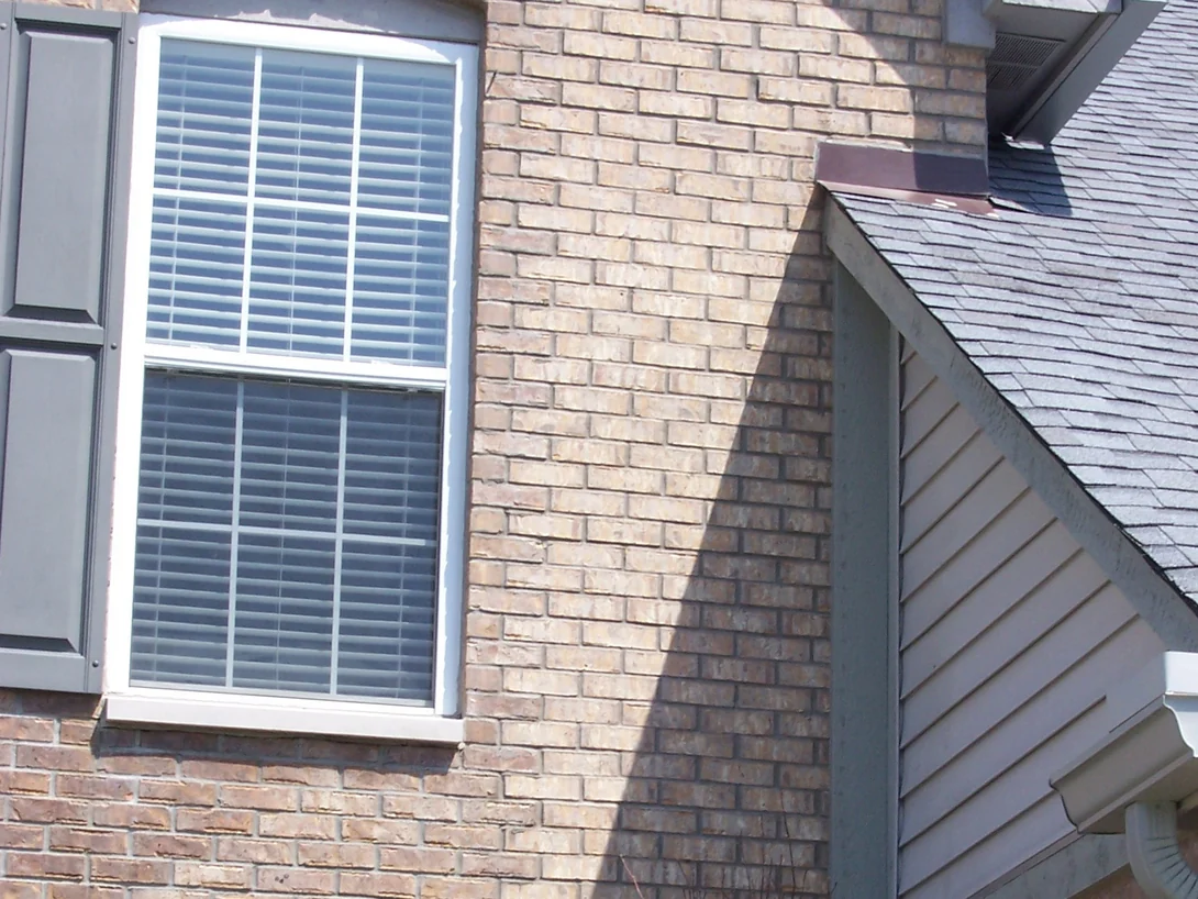 A shuttered upper window and the gable dormer beside it in 2008, pale and grey-cast units scattered through the buff and tan brick around them
