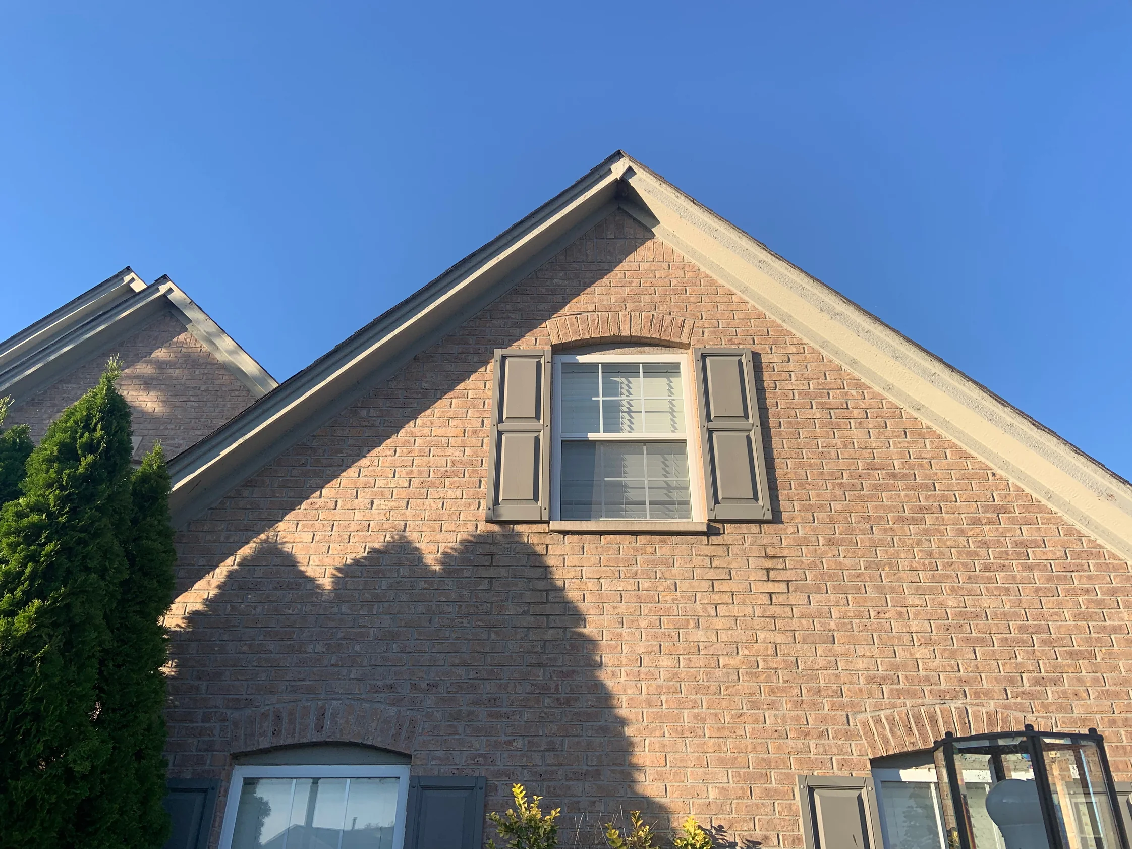 The gable end of the house in 2019 seen from below, the brick running as one tan and brown range from the eaves down past a shuttered window