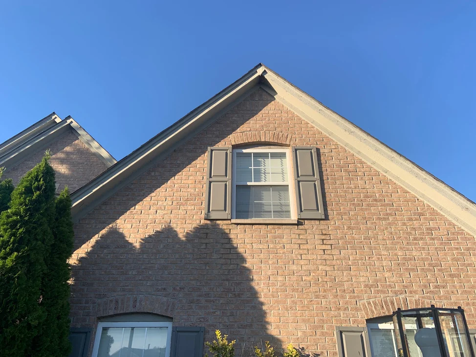The gable end of the house at Shadow Lake in 2019, its brick reading as one tan and brown range from the eaves down past a shuttered window.