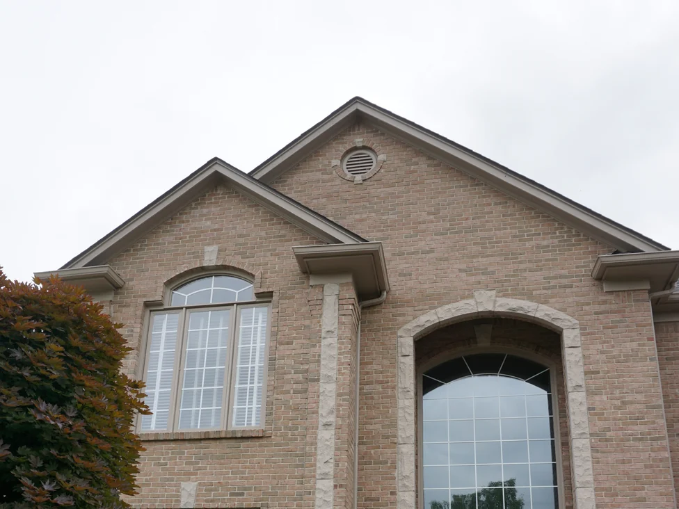The entry gable and the tall arched window from below in 2019, the brick one consistent tan range from the ridge down past the cast stone quoins