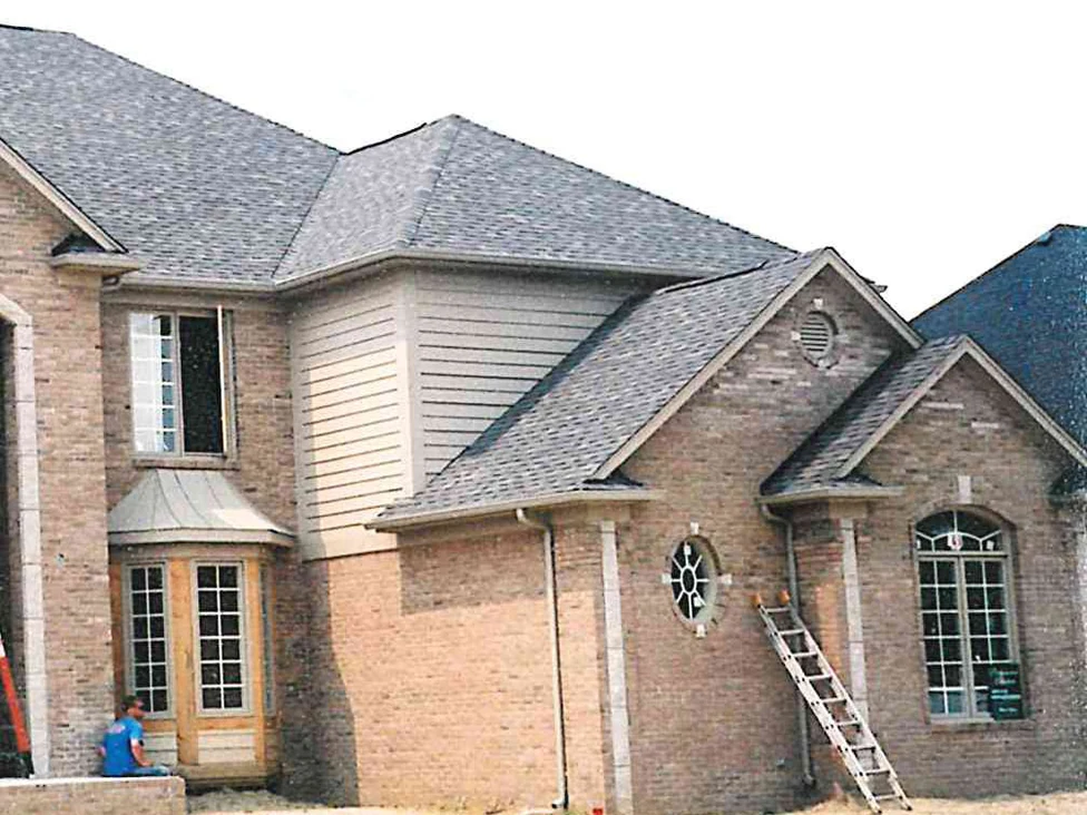 The right side of the house still under construction in 2002, its brick a pale uneven tan around a bay window, an oval window and an arched window, with bare soil where the lawn will go