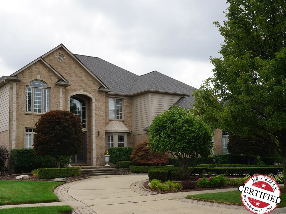 The house from its driveway in 2019, the brick reading as one even tan and cream range across the gables, the arched entry and the wing beyond.