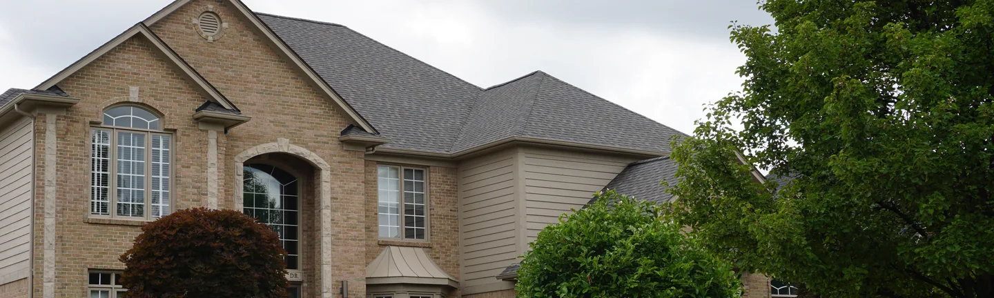 A two-story brick house seen from its driveway in 2019, the brick one even tan and cream range across the gables and the arched entry