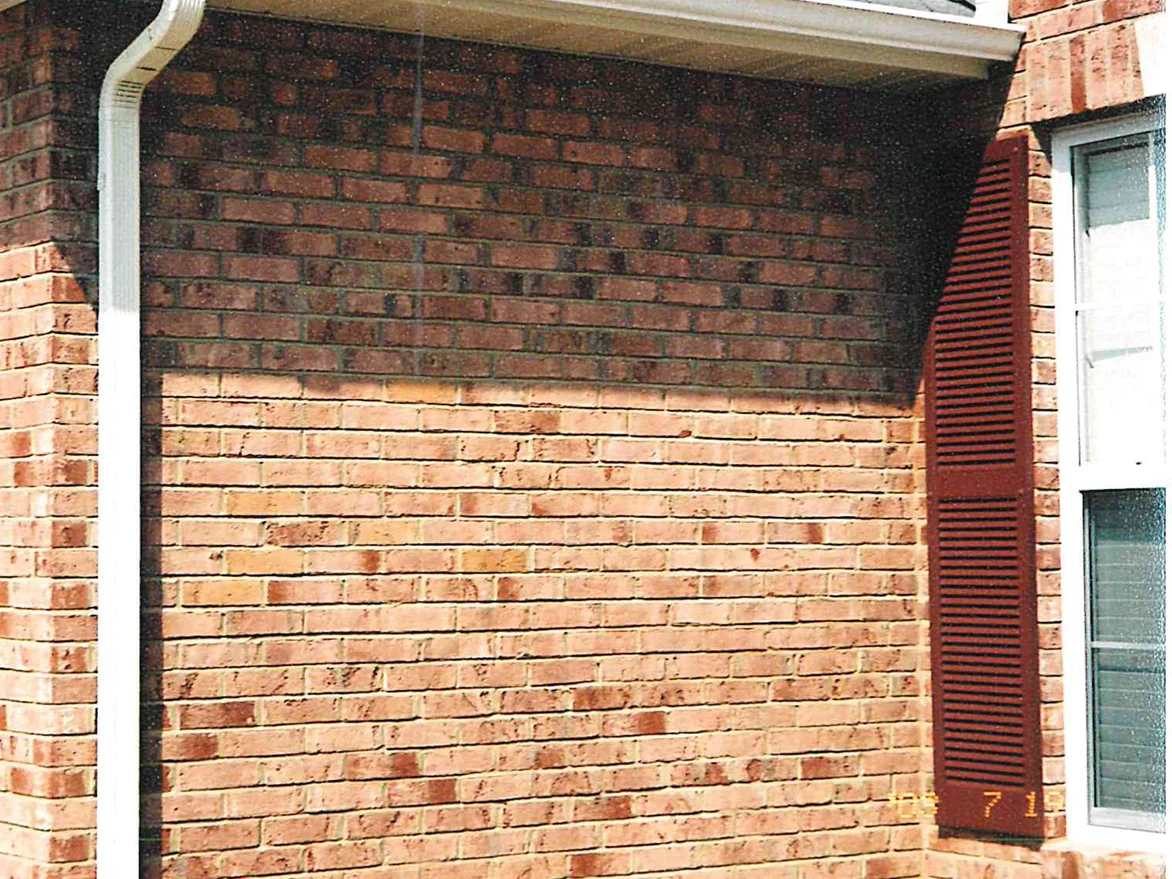 An outside corner of the house in 2003 after the stain, the brick a light peach and tan range with the roof overhang throwing a hard shadow across the top courses